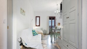 A hotel room with a bed, a small table, a chair, a wardrobe, and a view of the sky through a window.