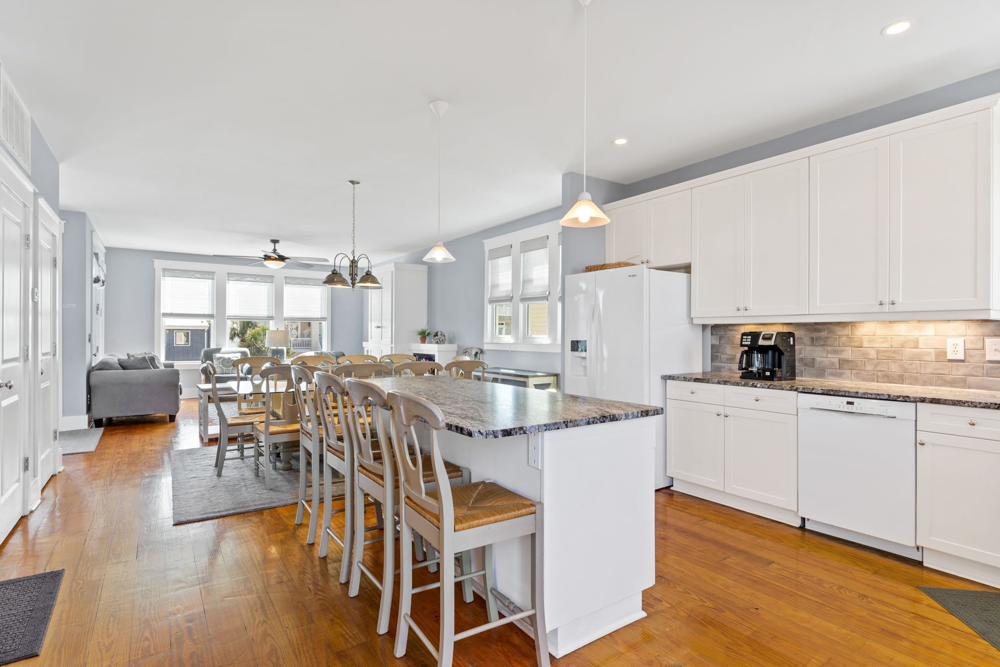 A modern kitchen with white cabinets, a granite countertop island, and a dining area with wooden chairs.