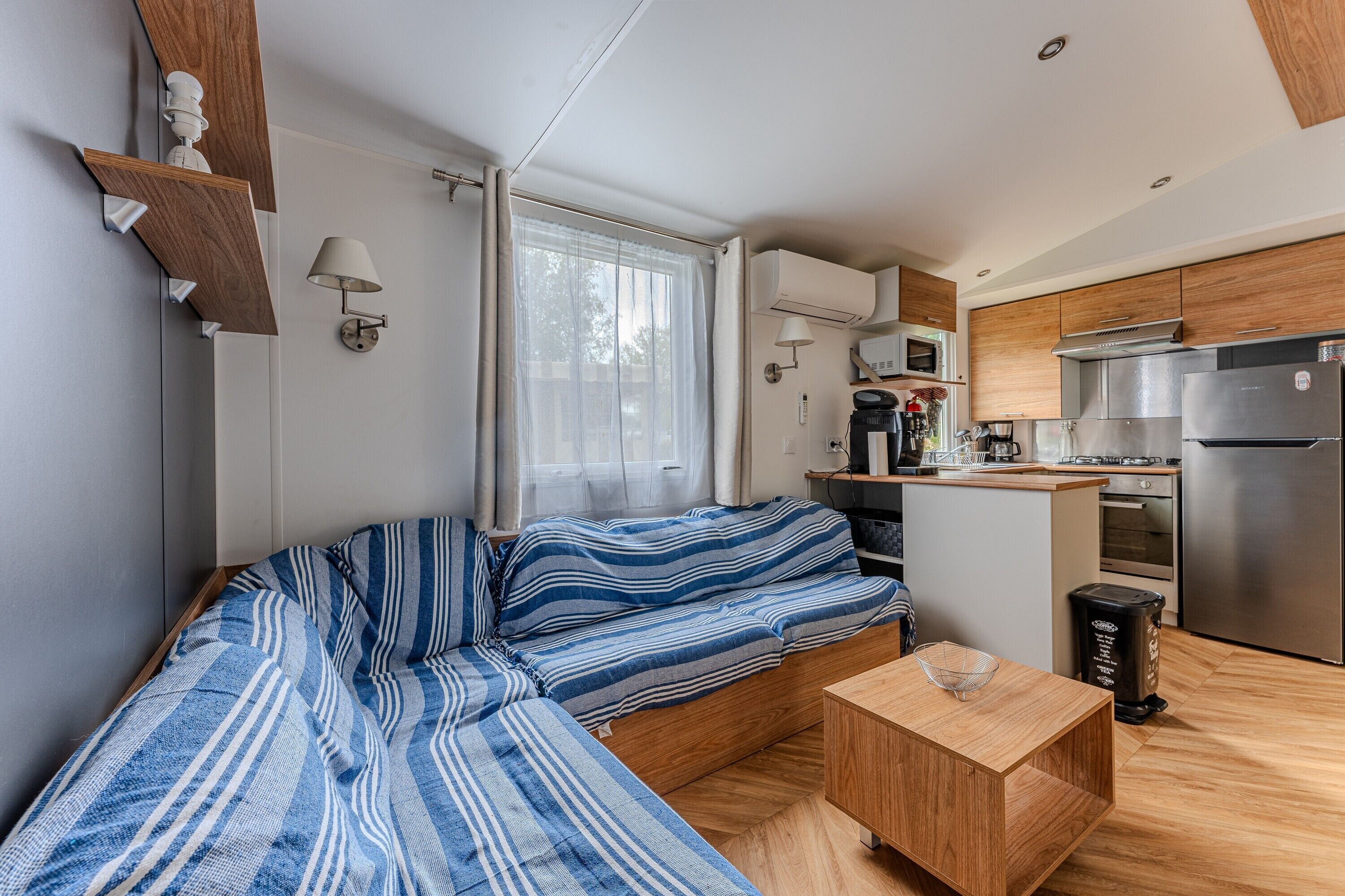 A compact living space with a sofa, a small table, a kitchenette, and a window with curtains.