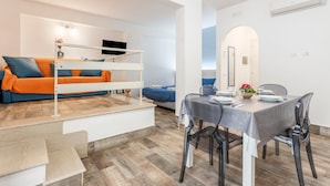 A modern room with a bunk bed, a dining table set for two, and a small kitchen area.