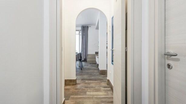 A narrow hallway with a tiled floor, a door on the right, and a staircase at the end.