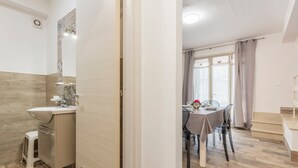 A modern bathroom with a sink, toilet, and shower. Adjacent is a dining area with a table and chairs.