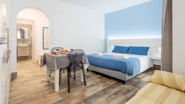 Quarto de hotel com cama, mesa com frutas, uma cadeira e um sofá.