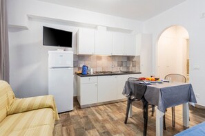 A compact kitchen with white cabinets, a built-in TV, and a dining area with a table set for two.