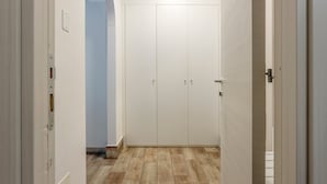 Um corredor com um guarda-roupa branco, um interruptor de luz e chão de azulejos.