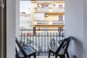 A balcony with two chairs, a view of parked cars, and a building with balconies and windows.