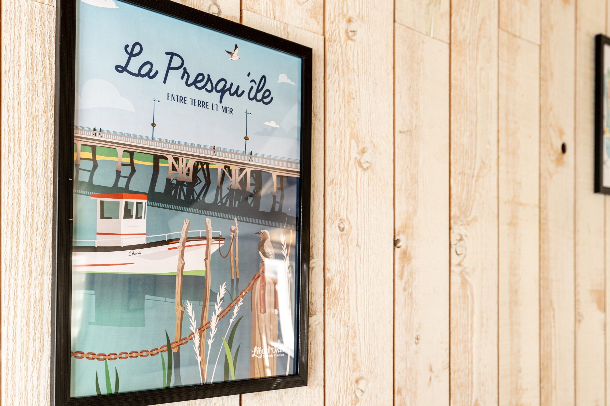 Un cuadro con un puente, el texto 'La Presqu'ile ENTRE TERRE ET MER' y un pájaro.