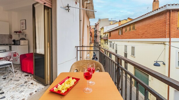 Een balkon met een tafel, twee glazen rode wijn en een bord chips.