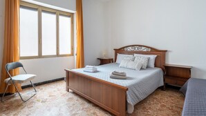 A bedroom with a wooden bed, a chair, a nightstand, and a window with curtains. - Vacation Home "Jerzu Centro 2" with Private Terrace & Balcony (Jerzu)