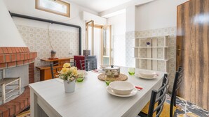 A kitchen with a dining table set for four, a brick oven, and a wooden door. - Vacation Home "Jerzu Centro 2" with Private Terrace & Balcony (Jerzu)
