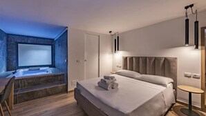 Habitación de hotel moderna con una cama grande, una mesita pequeña, un banco y una bañera de hidromasaje.