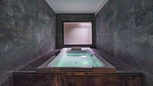 Un baño moderno con una bañera independiente, una ventana y paredes de piedra oscura.