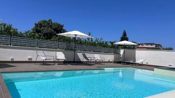 Ein Swimmingpool mit Liegestühlen und Sonnenschirmen, umgeben von einem weißen Zaun und Bäumen.