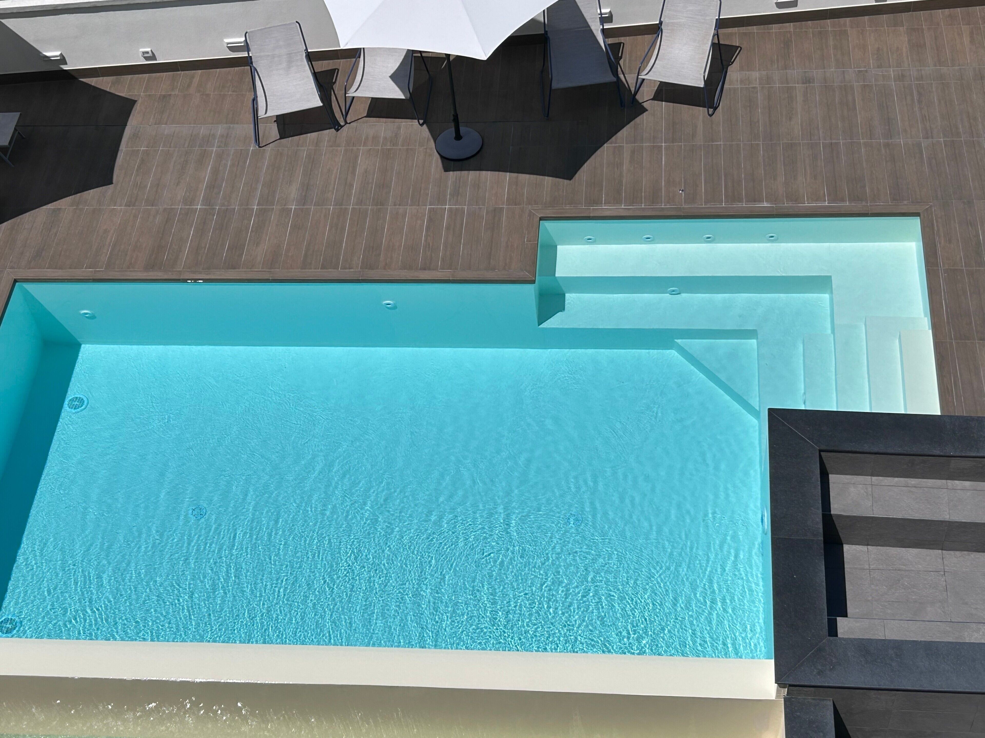 Una piscina en la azotea con superficie de agua azul cristalina, rodeada por una terraza de madera y zona de estar al aire libre.