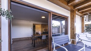 Un área de comedor al aire libre y de diseño moderno, con una mesa, sillas, un banco y un ventanal corredera que da a un espacio interior.