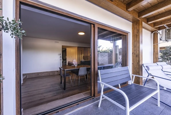 A modern outdoor dining area with a table and chairs, a bench, and a sliding glass door leading to an interior space.