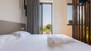 Habitación de hotel con cama, ventana con vistas a la vegetación y un balcón.