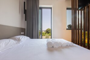 Hotellihuone, jossa on sänky, ikkuna, josta avautuu näkymä vehreään maisemaan, ja parveke.