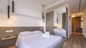 Una habitación de hotel moderna con una cama grande, mesitas de noche, un espejo y vistas al pasillo.