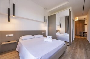 Moderni hotellihuone, jossa on suuri sänky, yöpöydät, peili ja näkymä käytävään.