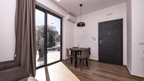 Una sala de estar moderna con un amplio ventanal corredera, un comedor con mesa y sillas, y una puerta de madera oscura.