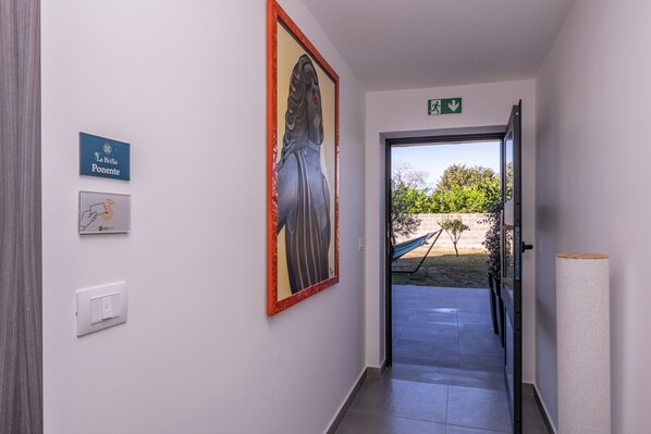 A hallway with a framed artwork, a sign reading 'La Brisa Ponente,' a light switch, and an exit sign.