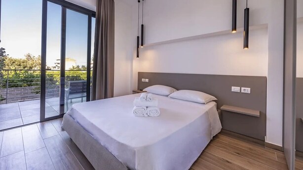 Una habitación de hotel moderna con una cama grande, un ventanal de vidrio a un balcón y un diseño minimalista.