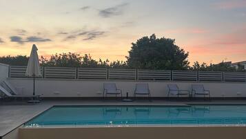 Ein Schwimmbecken mit Liegestühlen und Sonnenschirm, umgeben von einer niedrigen Mauer und Bäumen.