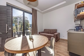 Uma sala de estar moderna com uma mesa redonda de madeira, um sofá e uma área de cozinha com micro-ondas.