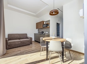 A modern living space with a sofa, a round dining table with chairs, a kitchen area, and a pendant light.