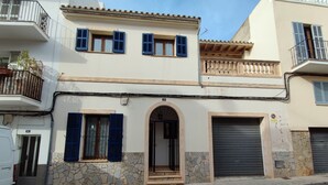 Un edificio de dos pisos con fachada de piedra, una entrada central con arco y un balcón con barandilla.