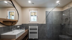 Une salle de bain moderne avec un meuble-lavabo en bois, un lavabo blanc, une cabine de douche en verre et une fenêtre offrant une vue agréable.