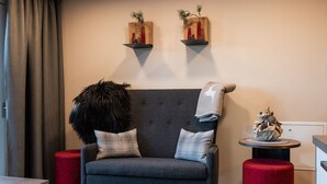 Un salon moderne avec un canapé gris, des poufs rouges et des étagères murales ornées d’objets décoratifs.