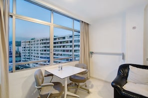 A room with a large window, a white table, two chairs, a black leather sofa, and a view of a multi-story building. - Vacation Apartment 'Los Molinos 538' with Sea View, Private Pool and Wi-Fi (Maspalomas)