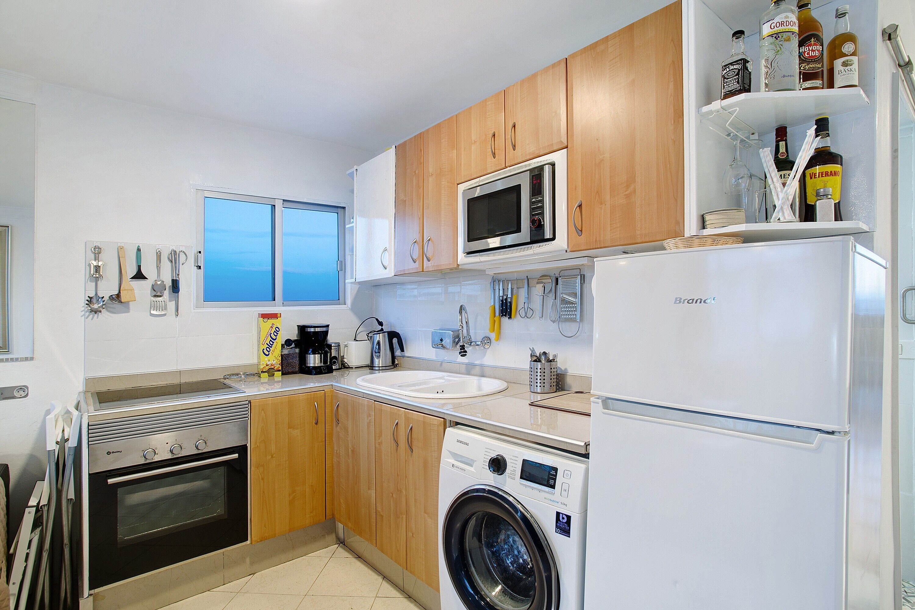 A compact kitchen with a microwave, oven, sink, and washing machine.