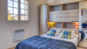 Ein Schlafzimmer mit Bett, Fenster, Nachttischlampe und integriertem Kleiderschrank.