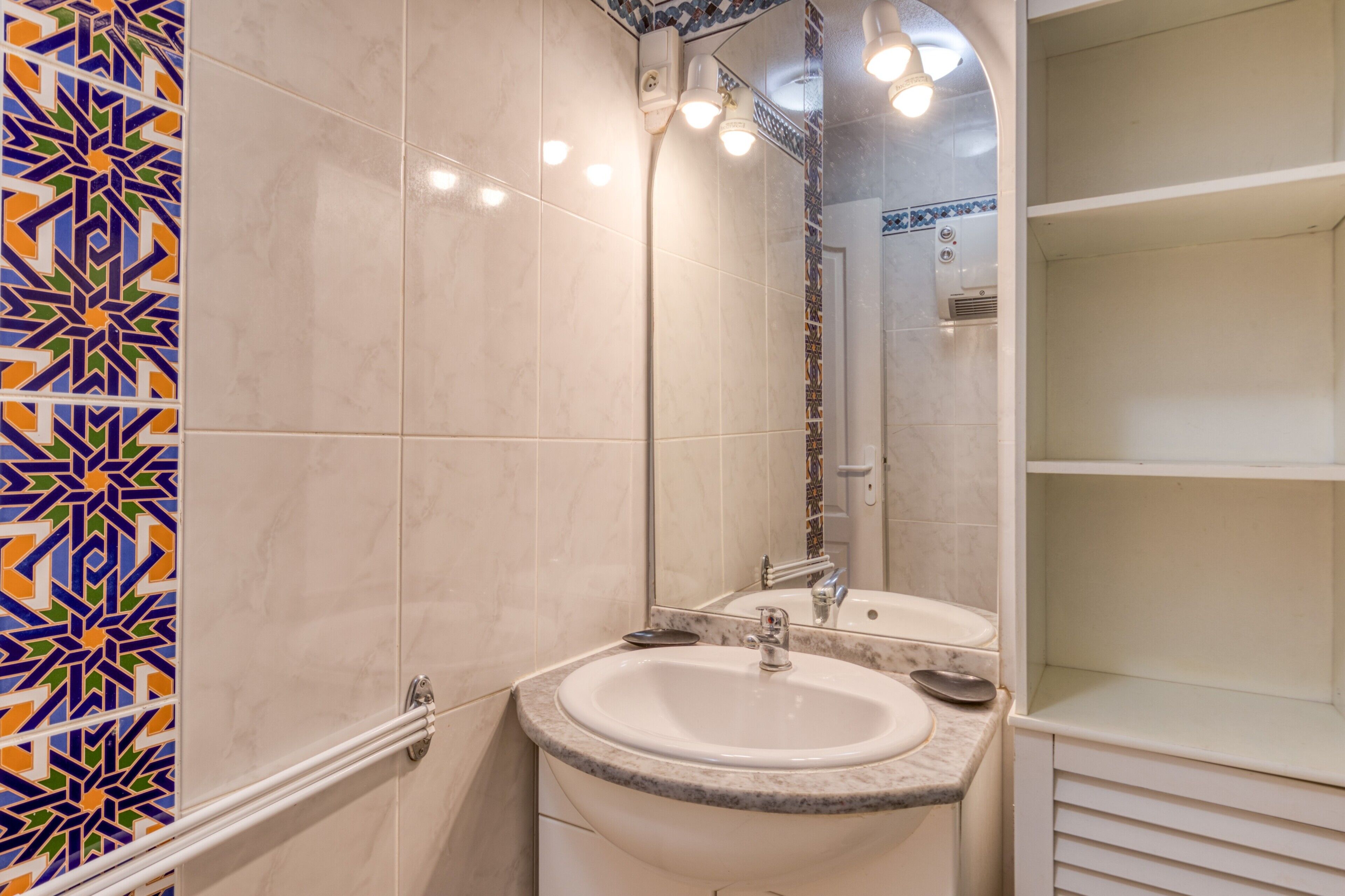 A bathroom with a sink, mirror, and tiled walls.