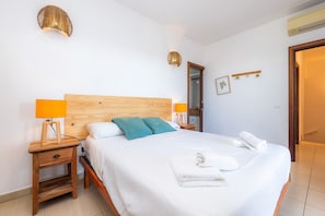 Ein ordentlich bezogenes Bett mit weißen Leinen, zwei Nachttischlampen, ein Holz-Kopfteil und ein kleiner Nachttisch mit einer Lampe.