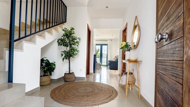 Un escalier menant à un deuxième étage, un couloir avec une porte en bois et une vue sur un espace de vie.