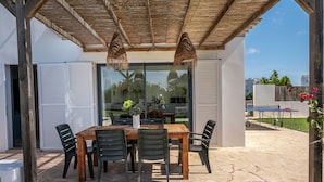 Une terrasse extérieure avec une table et des chaises en bois, une porte vitrée et un espace abrité doté d’un plafond en bois.