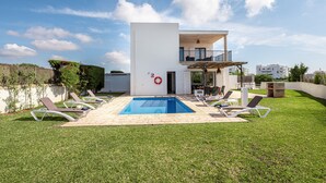 Une maison moderne à deux étages, dotée d’une piscine, de chaises longues et d’un balcon.