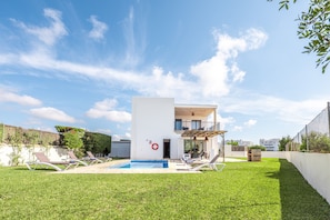 Ein modernes, zweistöckiges Haus mit Swimmingpool, Liegestühlen und einem Balkon.