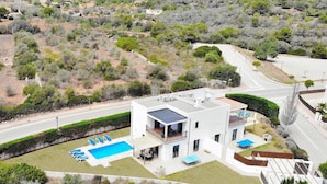 Une maison moderne à deux étages, dotée d’une piscine, d’un patio couvert et offrant une vue sur le paysage environnant.