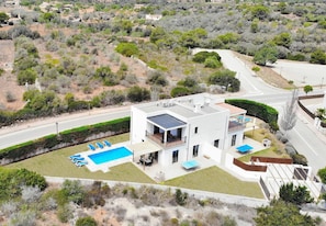 A modern two-story house with a swimming pool, a covered patio, and a view of the surrounding landscape.