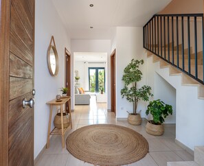 A hallway with a wooden door, a round woven rug, a small wooden table with a basket, and a staircase with a black railing.