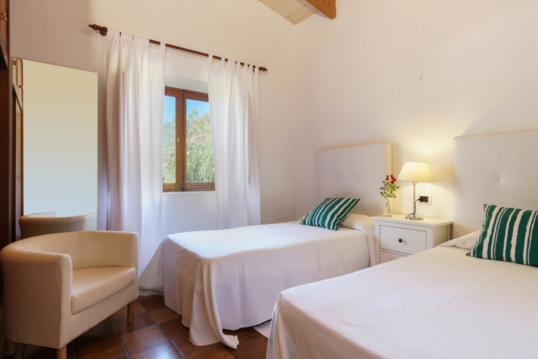 Une chambre d’hôtel avec deux lits simples, une chaise, une table de chevet avec une lampe et une fenêtre avec des rideaux.