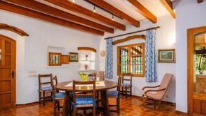 Uma sala de jantar com uma mesa e cadeiras de madeira, uma cadeira de balanço e uma janela com cortinas.