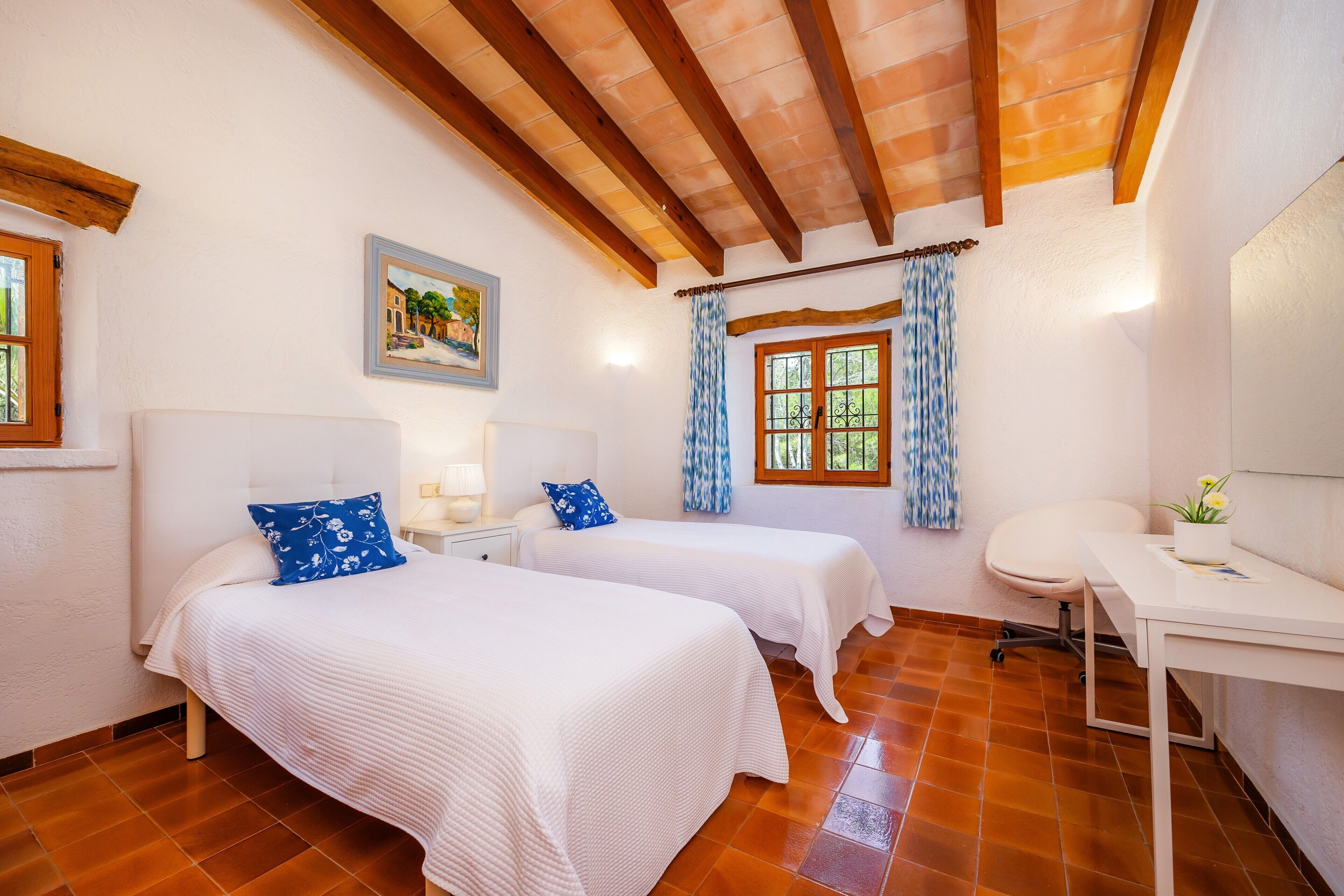 Una habitación con dos camas, un escritorio, una silla, una ventana con cortinas y un cuadro en la pared.