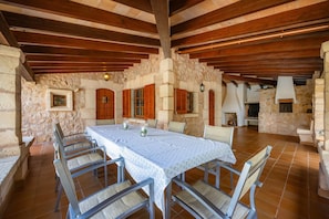 A rustic dining area with a stone wall, wooden beams, and a long table with chairs. - Villa "Can Seguinot d'Alt" with Mountain View, Private Pool & Wi-Fi (pollensa)