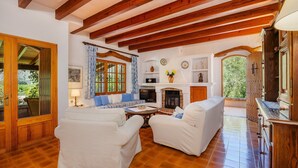 Uma sala de estar espaçosa, com vigas de madeira, lareira e vista para o verde.